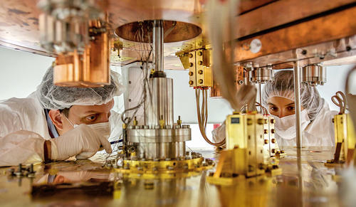 2 scientists in clean room garb looking inside CUORE detector.